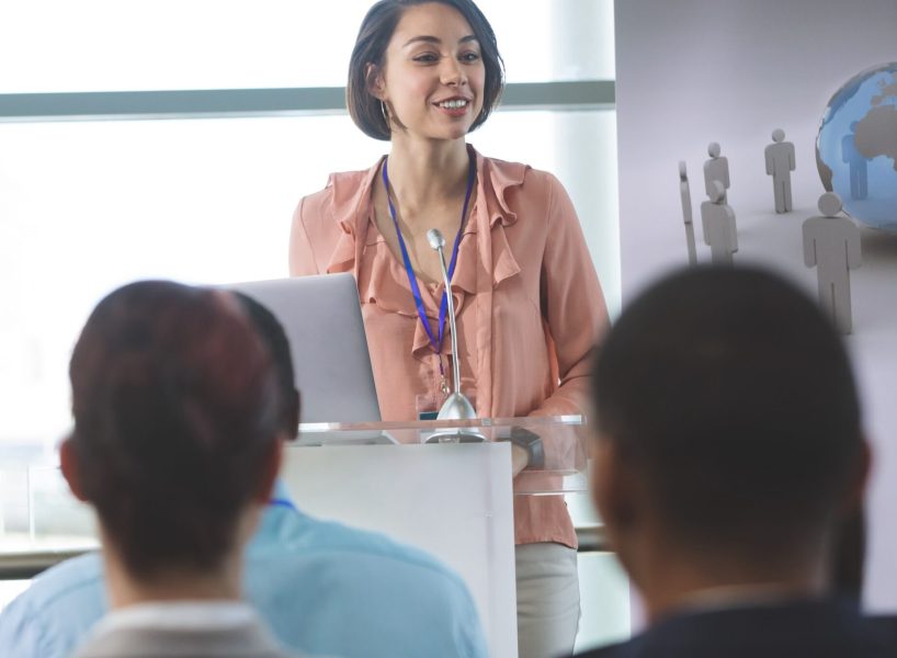 Front view of mixed-race female speaker with laptop speaks at a business seminar in office building